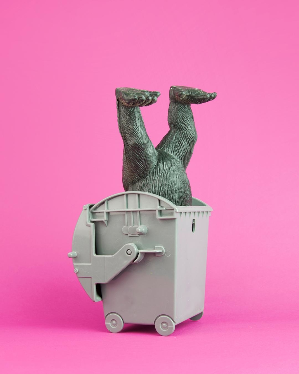 Affenfigur steckt kopfüber in Müllcontainer vor pinkem Hintergrund