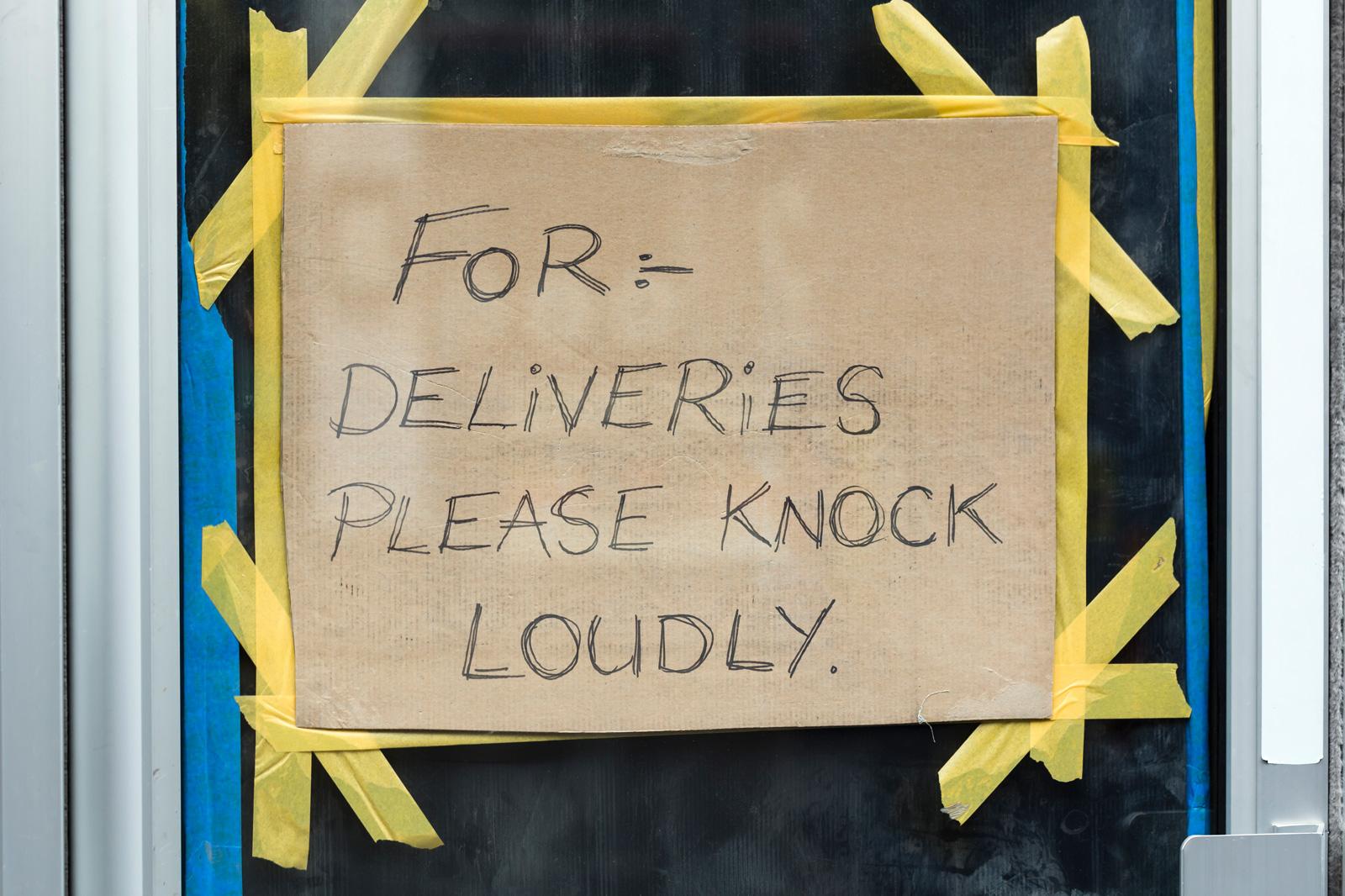 Pappschild an Glastür mit der Aufschrift: For deliveries please knock loudly